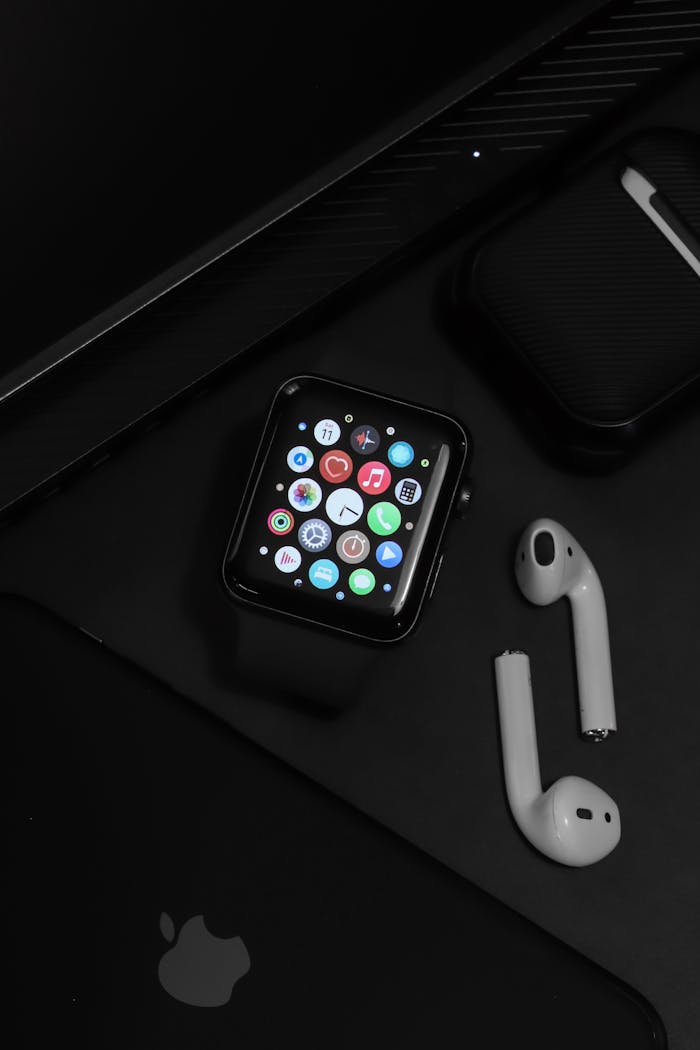 Stylish arrangement of modern tech gadgets on a dark surface, showcasing an Apple watch and AirPods.