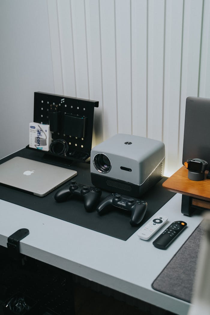 A sleek home office setup featuring a projector, game controllers, and laptop.